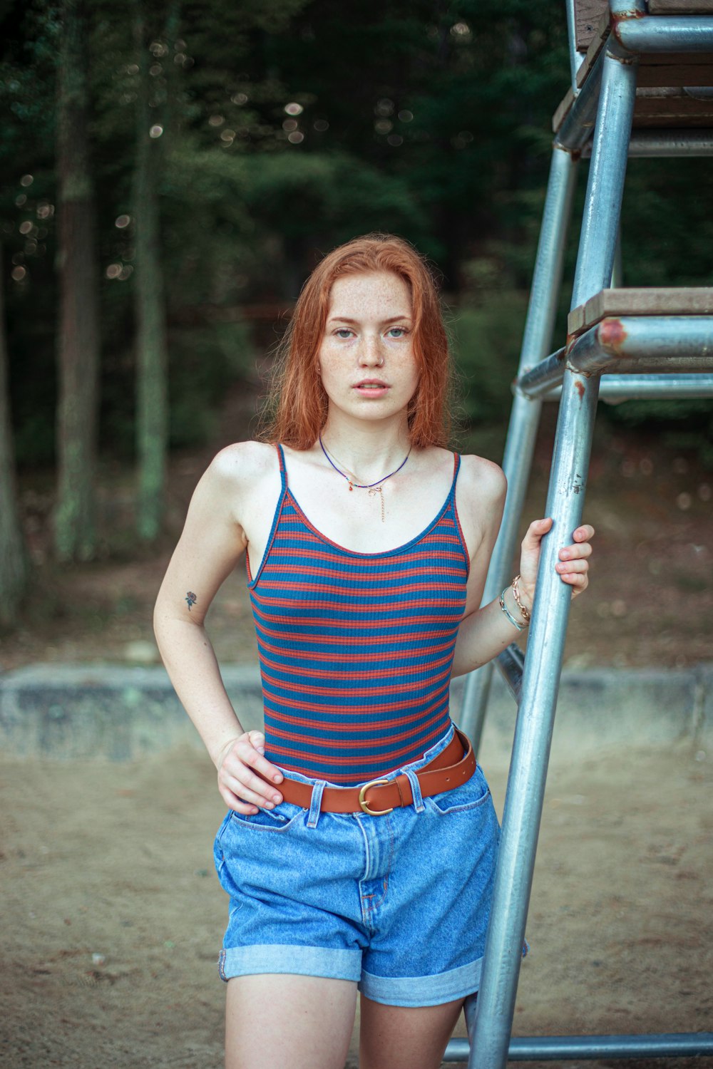 woman in blue and white stripe tank top and blue denim jeans standing beside gray metal