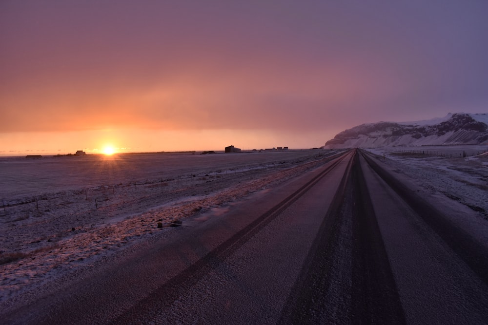 gray road between snow covered field during sunset