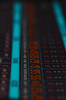 A close-up of an electronic display panel featuring numbers and text in a digital, pixelated format. The display includes both orange and blue segments, with various numbers and terms like 'MODE' and 'ATTACK' visible. The image conveys a sense of technology or computing, likely related to audio or technical equipment.