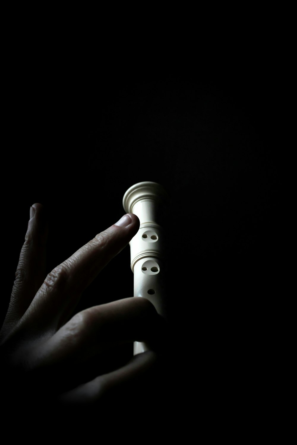 persona sosteniendo flauta blanca en cuarto oscuro