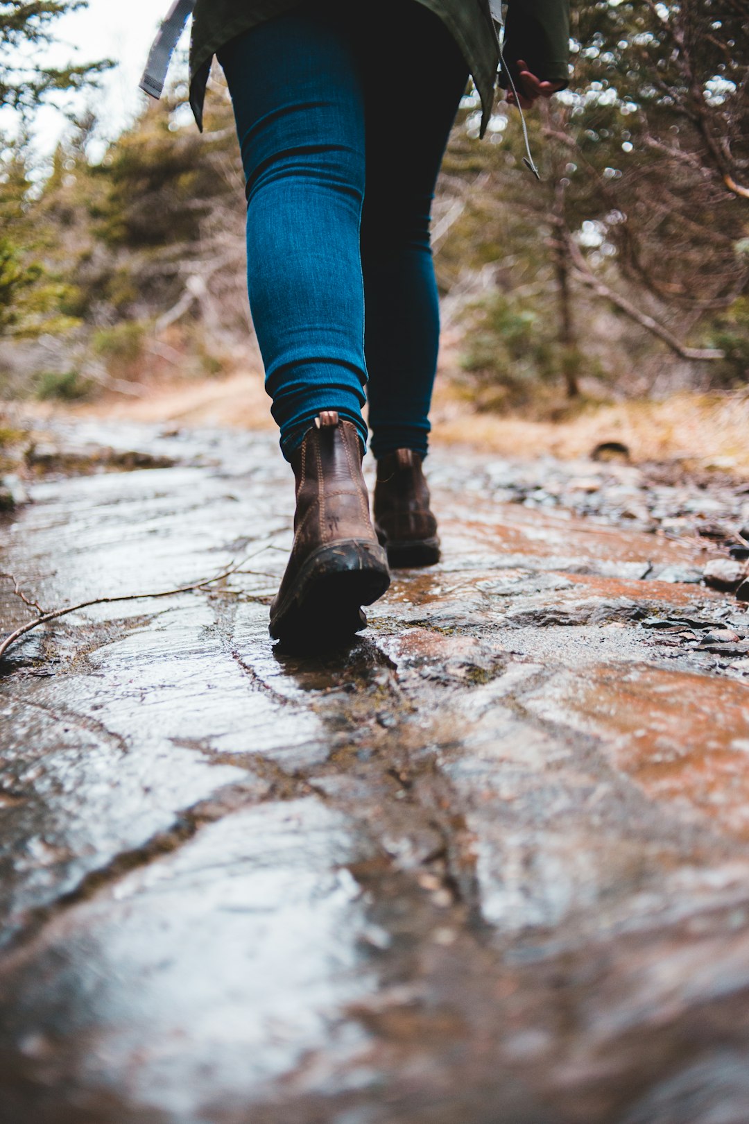 person in blue denim jeans and brown hiking boots standing on brown dried leaves