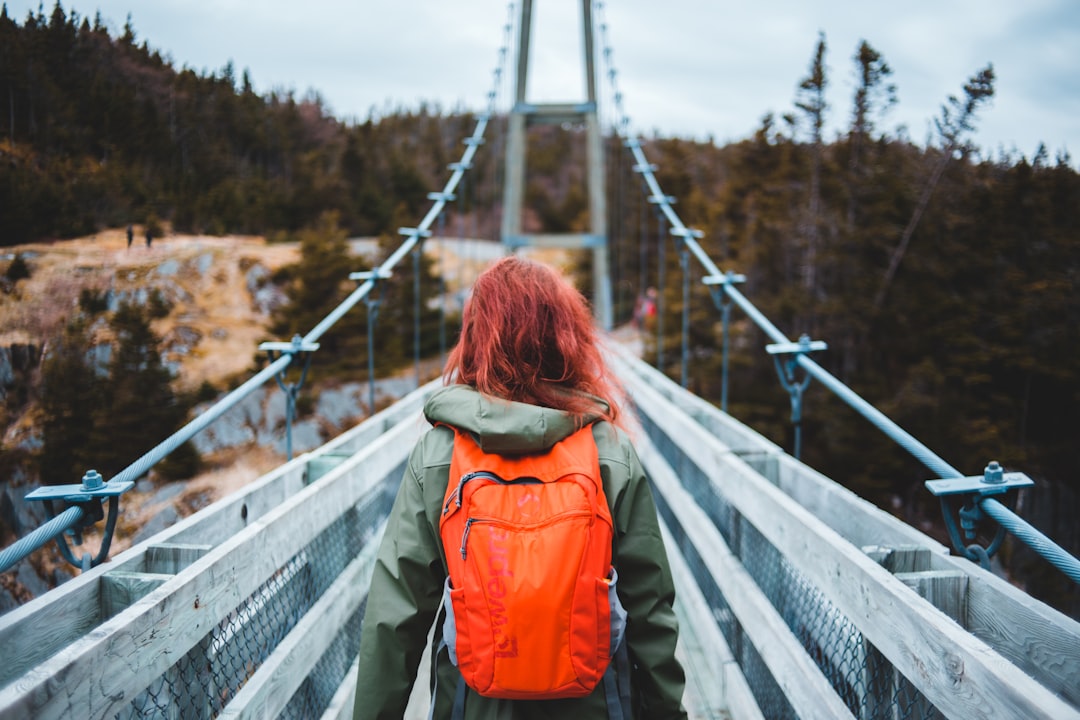 woman in orange jacket and blue denim jeans standing on bridge during daytime