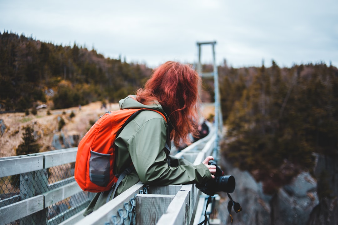 woman in gray jacket and orange backpack holding black dslr camera