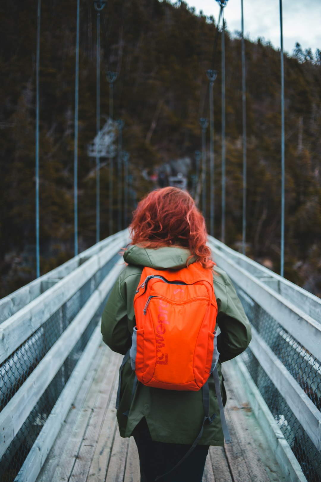 woman in orange and black jacket standing on bridge