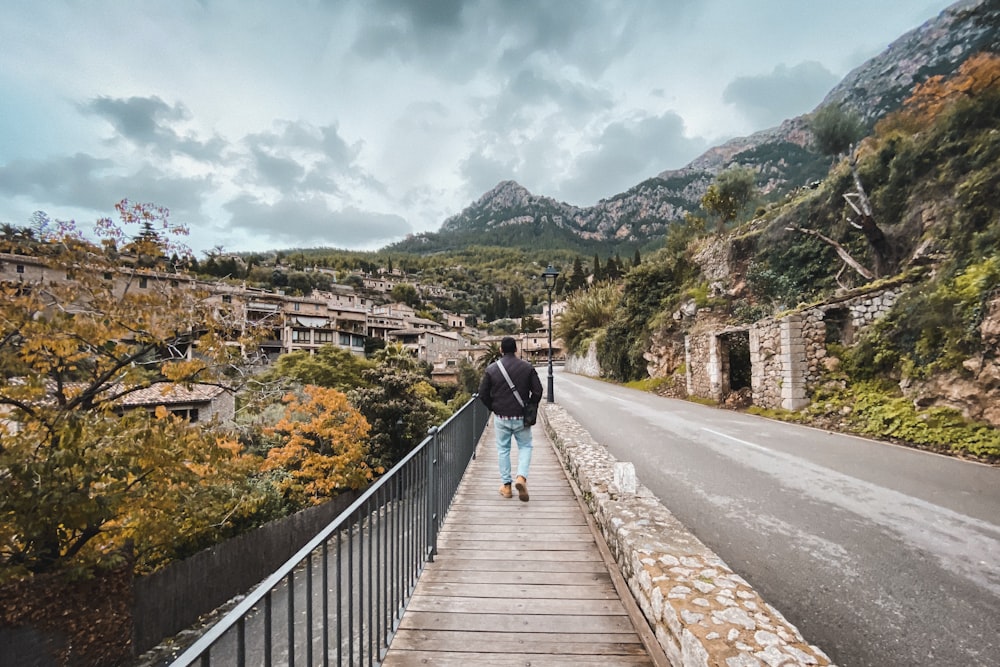 man in black jacket and blue denim jeans walking on brown wooden bridge during daytime