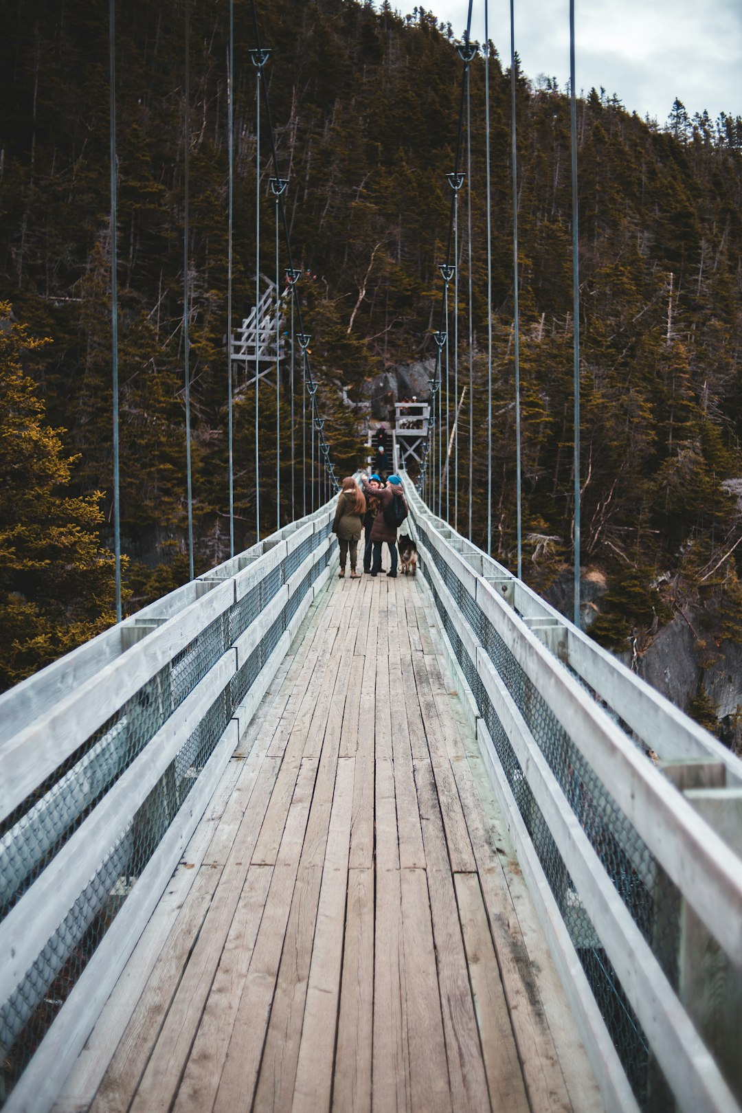 man in black jacket and brown pants walking on wooden bridge
