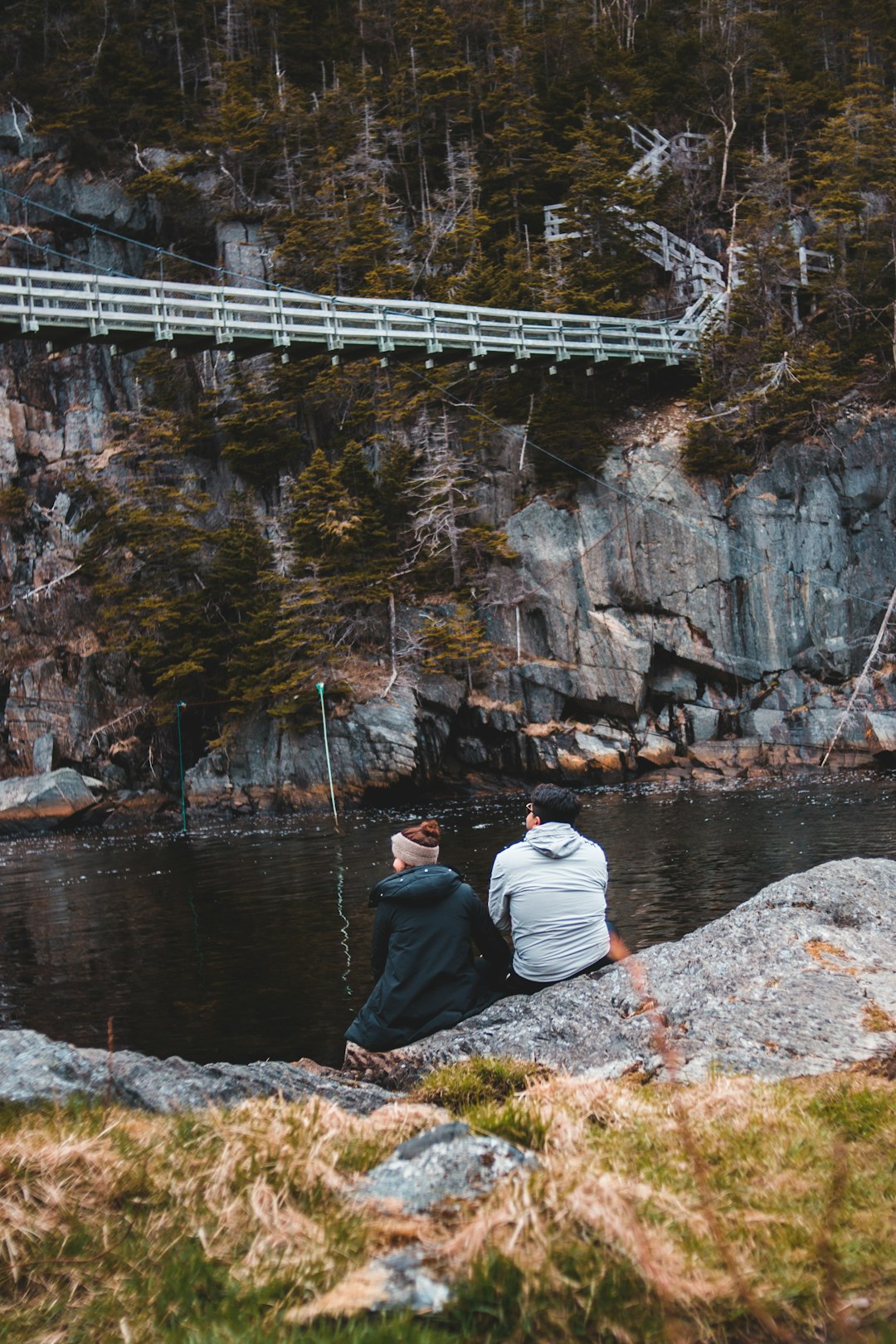 man in gray hoodie sitting on rock near body of water during daytime