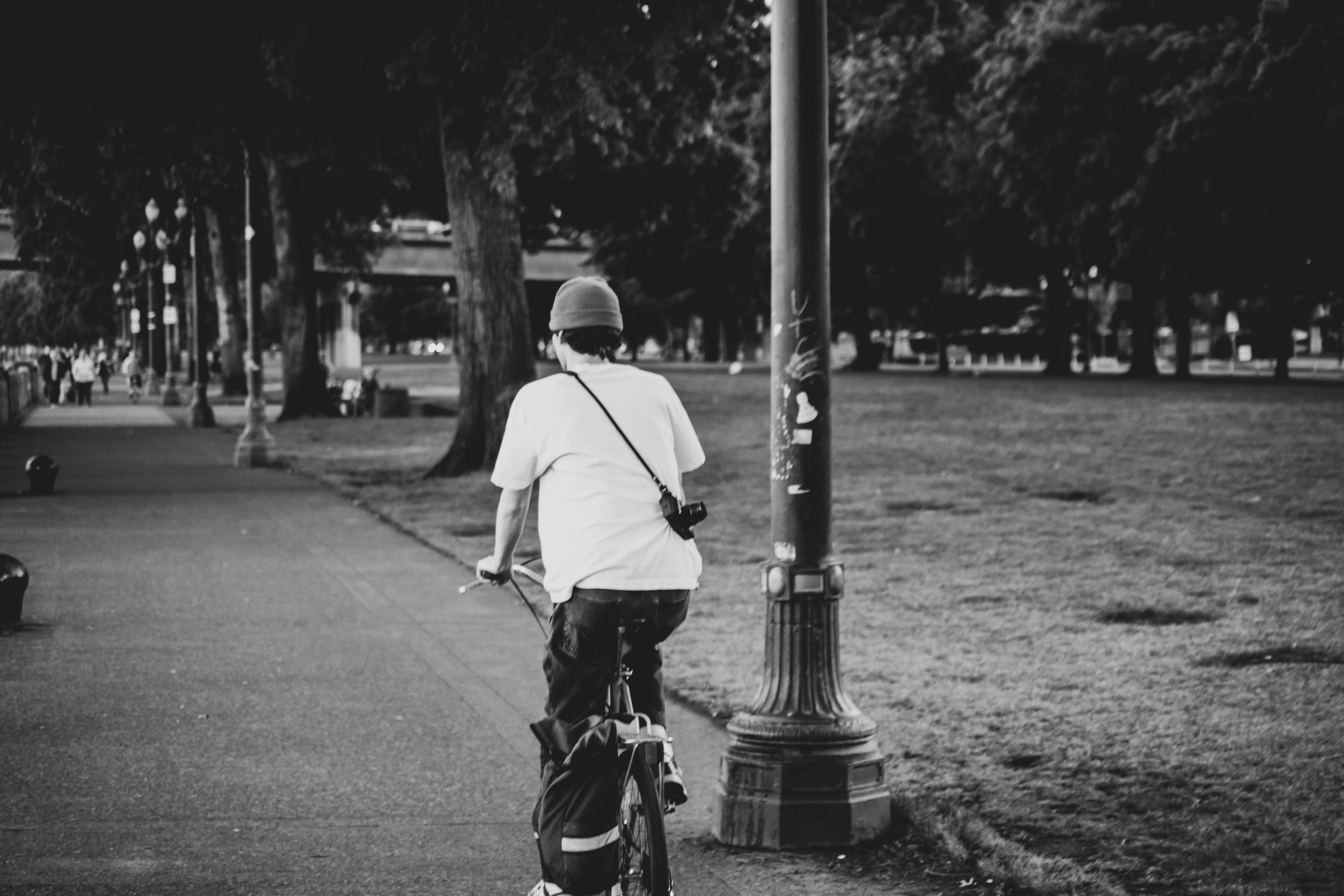 man in white shirt and black pants riding bicycle on road in grayscale photography