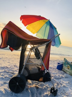 A vibrant beach scene with colorful umbrellas, coolers, and a foldable beach wagon packed with summer gear