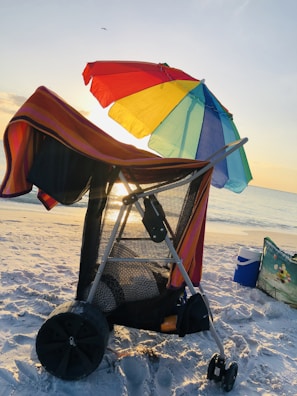 A vibrant beach scene featuring a colorful foldable cart loaded with picnic gear and coolers.