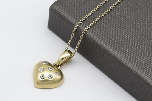 gold heart pendant necklace beside gray leather pouch