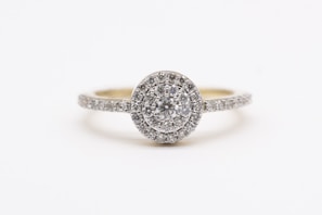 A sparkling diamond engagement ring with a round center stone surrounded by a halo of smaller diamonds, set on a band encrusted with additional diamonds.