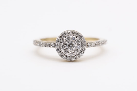 A sparkling diamond engagement ring with a round center stone surrounded by a halo of smaller diamonds, set on a band encrusted with additional diamonds.