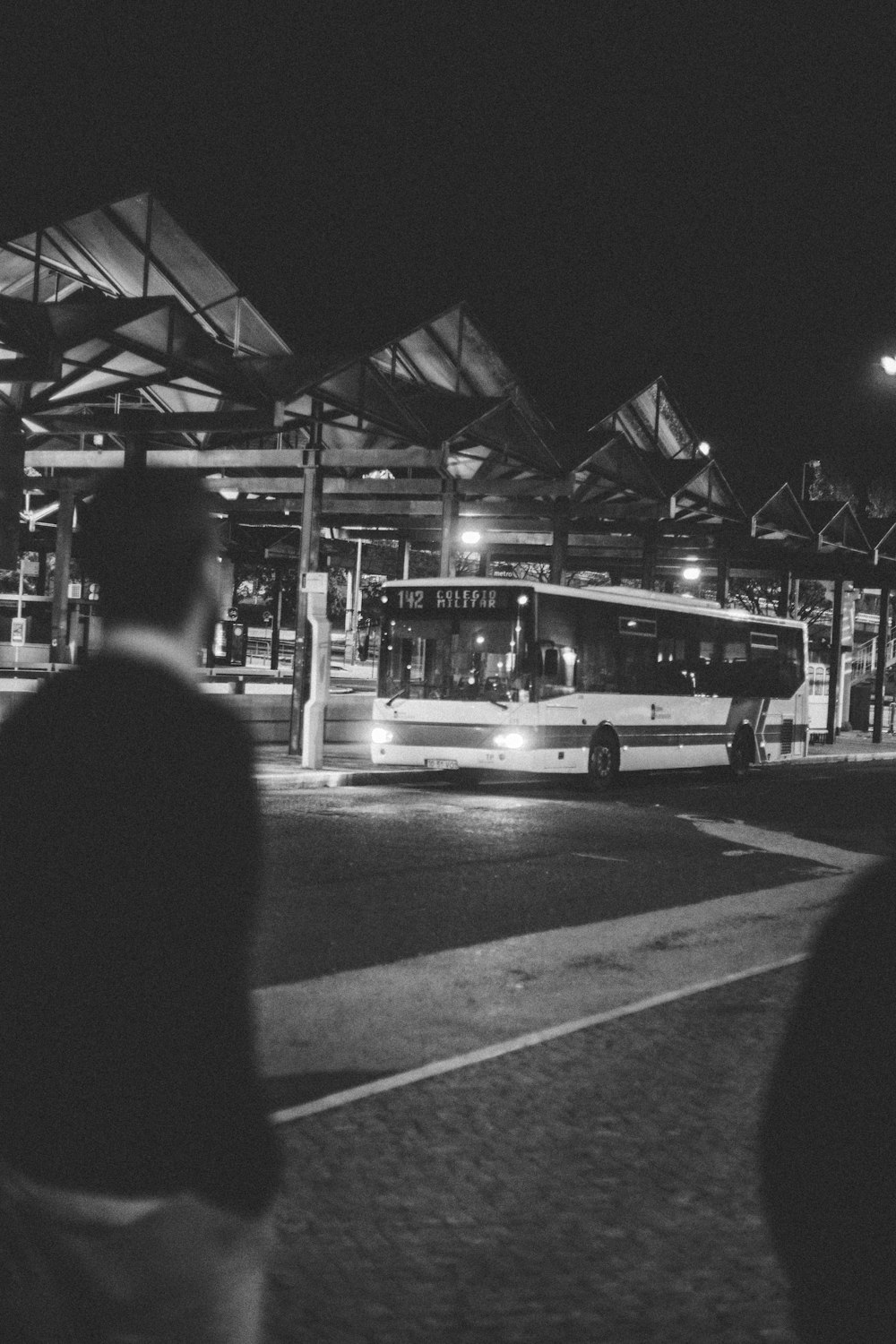 grayscale photo of man in black jacket standing near bus