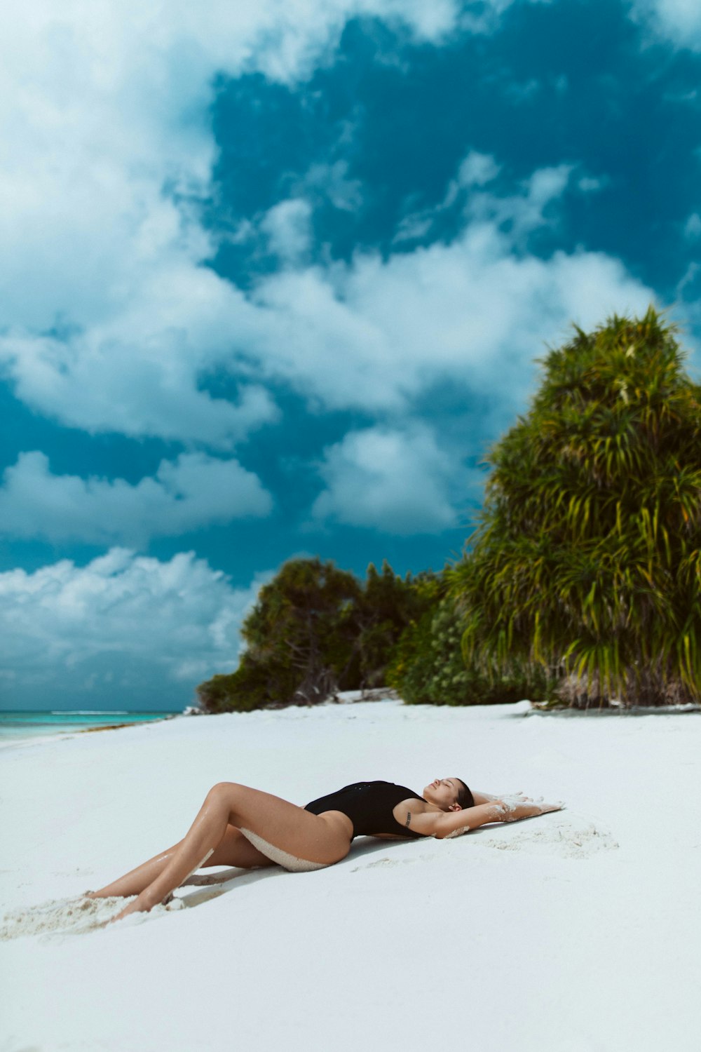 낮 동안 하얀 모래 해변에 누워 검은 비키니를 입은 여자
