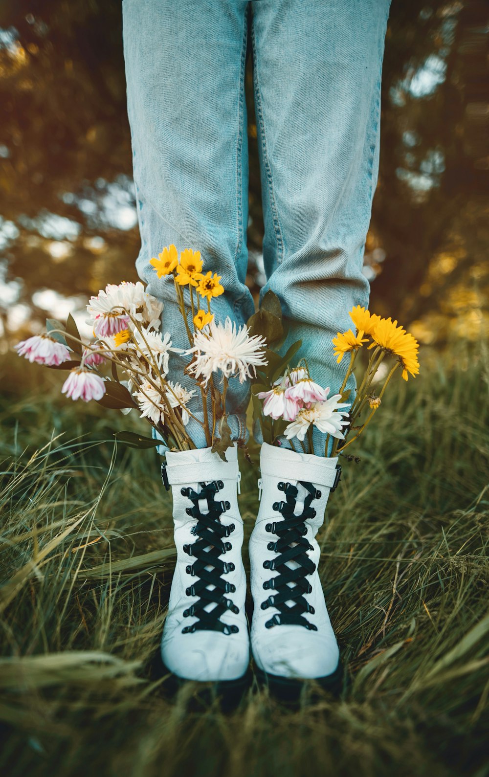 person in blue denim jeans and white and black boots holding white and yellow flowers
