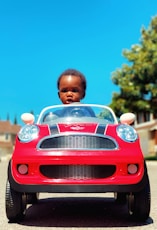 boy in white shirt standing beside red car