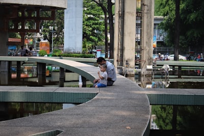 man in blue denim jacket sitting on gray concrete bench during daytime comic con zoom background