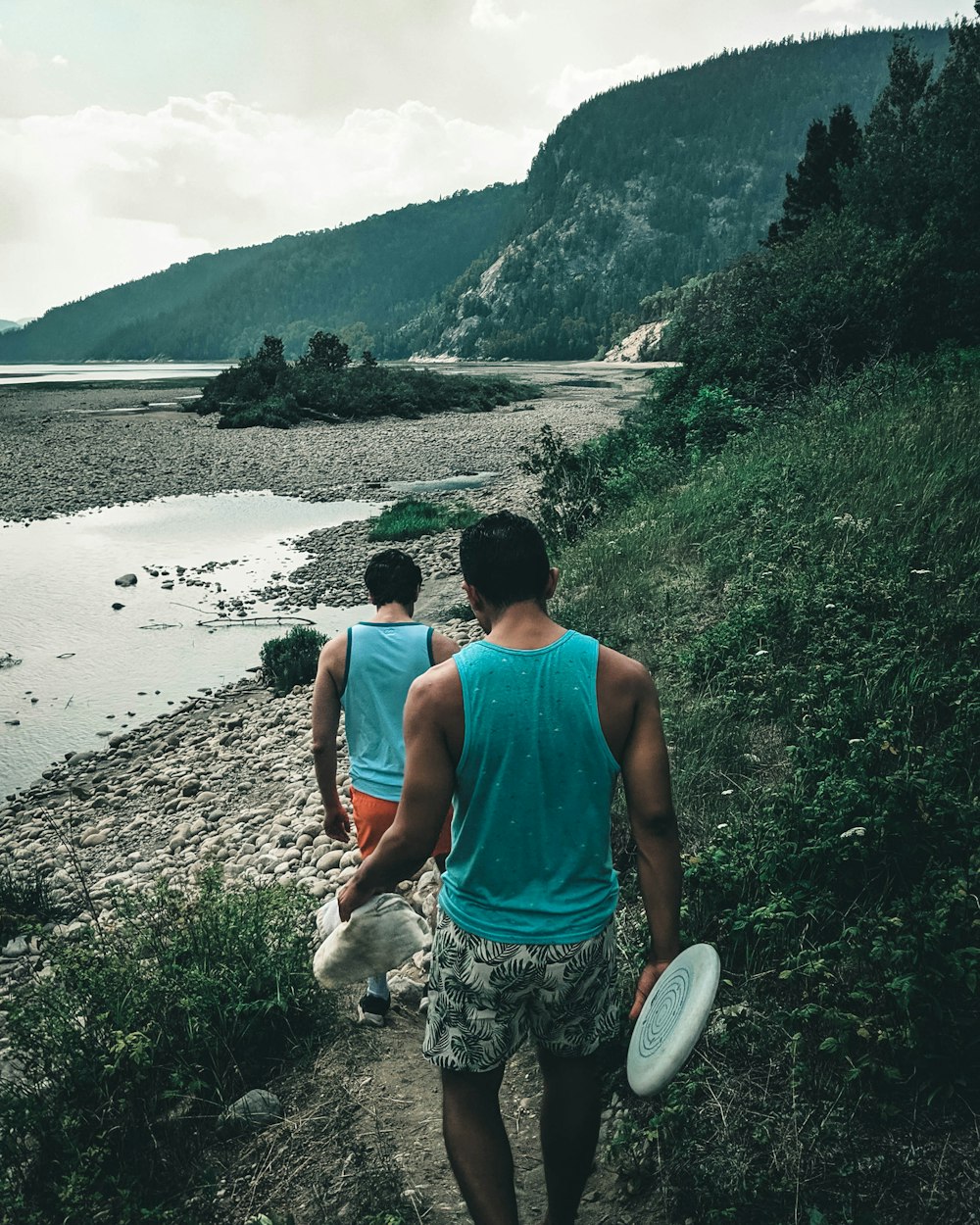 昼間、海岸に立つ青いタンクトップと灰色の短パンを着た男性