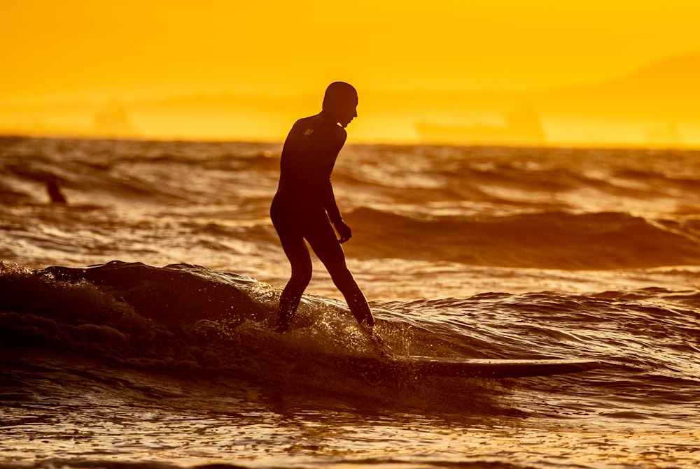 silhouette of man standing on sea shore during sunset