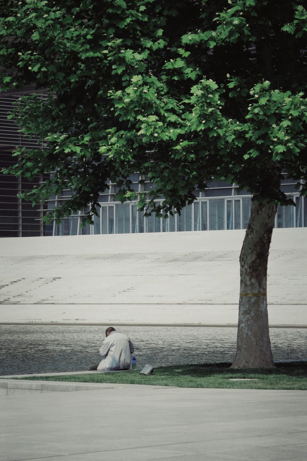 Uomo in thobe bianco che si siede sul pavimento di cemento grigio durante il giorno