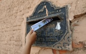 Close-up of hands placing a letter into a mailbox on a sunny street.