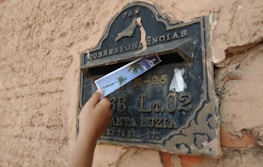 Close-up of hands placing a letter into a mailbox on a sunny street.