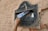 A hand is inserting a postcard into an old, rustic metal mailbox mounted on a textured wall. The mailbox is labeled with various inscriptions and numbers, suggesting its location and purpose.