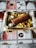 A rectangular tray filled with cooked diced potatoes and a rolled meat dish sliced to reveal stuffing, resting on a decorative tablecloth featuring coffee and food-themed images.