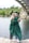 woman in green academic dress standing on gray concrete pavement during daytime