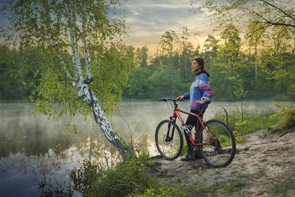 woman in blue shirt riding red and black mountain bike on river during daytime