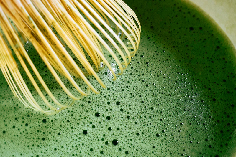 Batidor de bambú mezclando té matcha verde con espuma en un cuenco