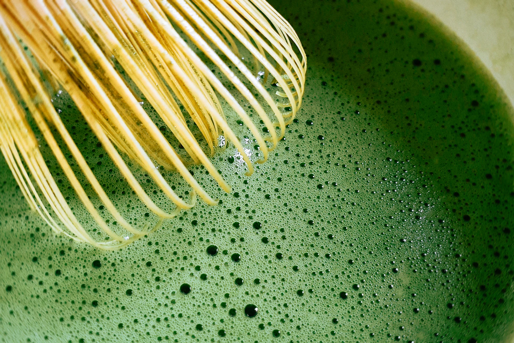 A bamboo chasen mid-whisk over a dark surface
