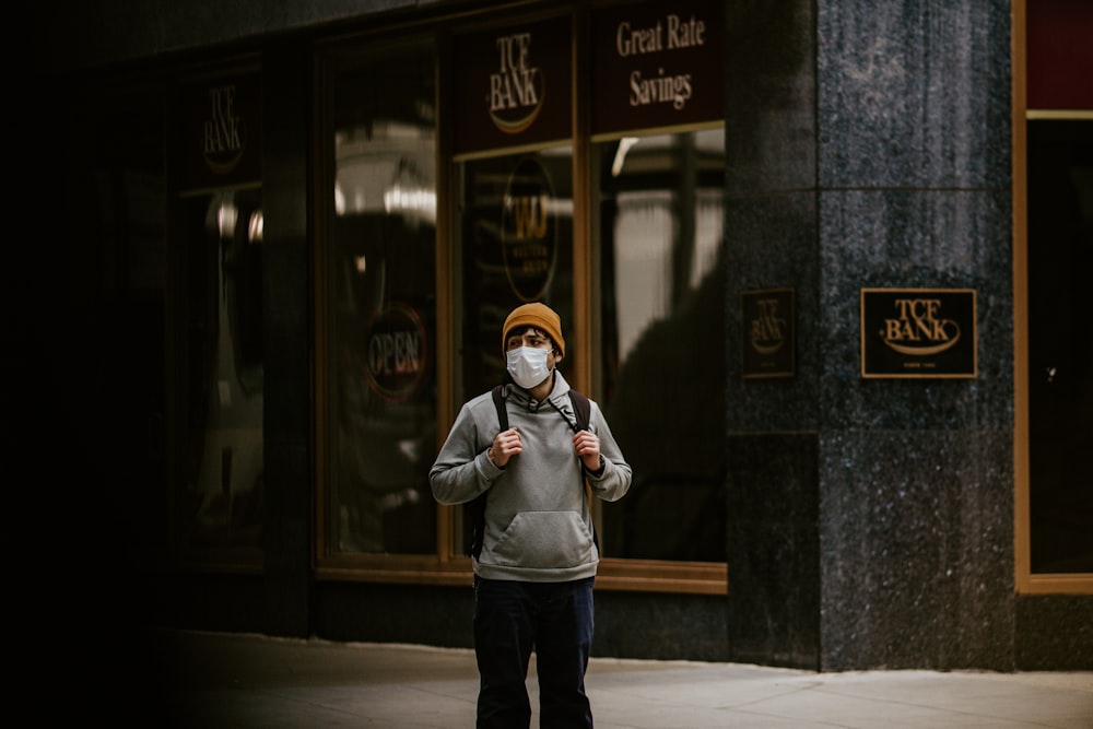 man in gray jacket and blue denim jeans standing beside building during daytime