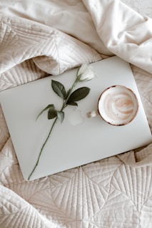 A soft lavender-themed photo showing a cozy workspace with a laptop, a delicate rosary, and a cup of tea.