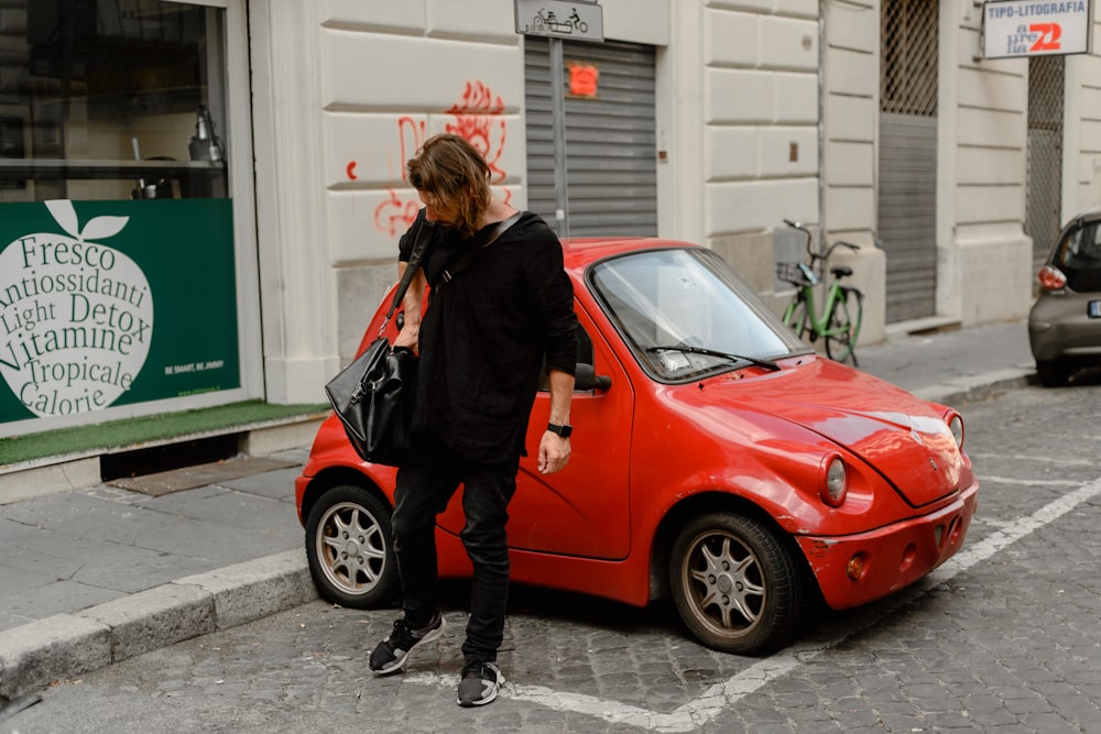 woman in black jacket and black pants standing beside red car