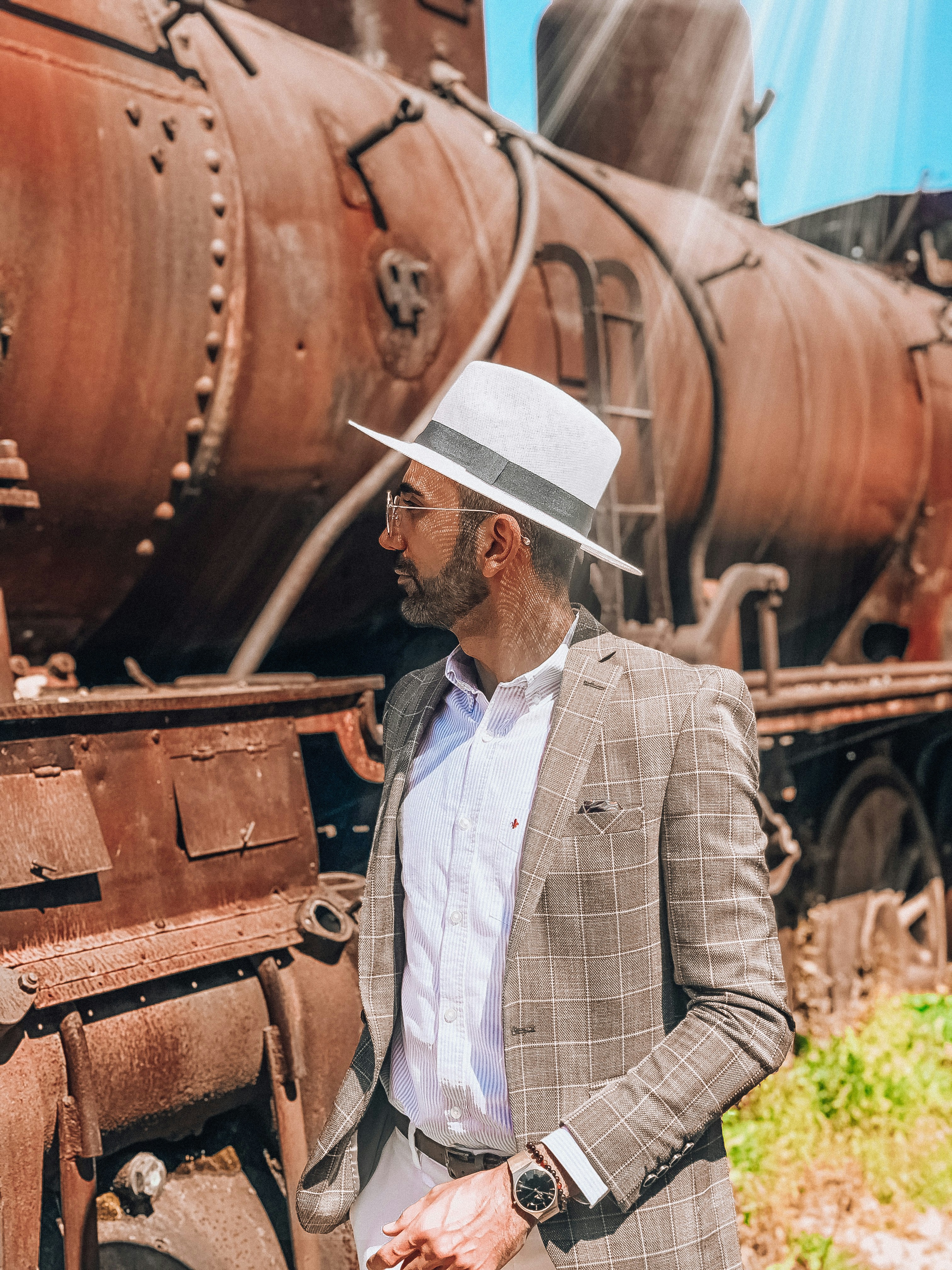 homem no chapéu branco e camisa social xadrez branca e preta de pé ao lado do trem marrom