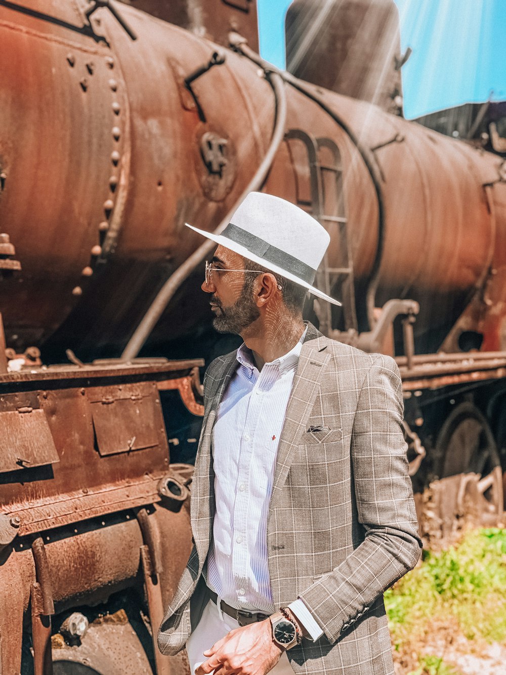 man in white hat and white and black plaid dress shirt standing beside brown train
