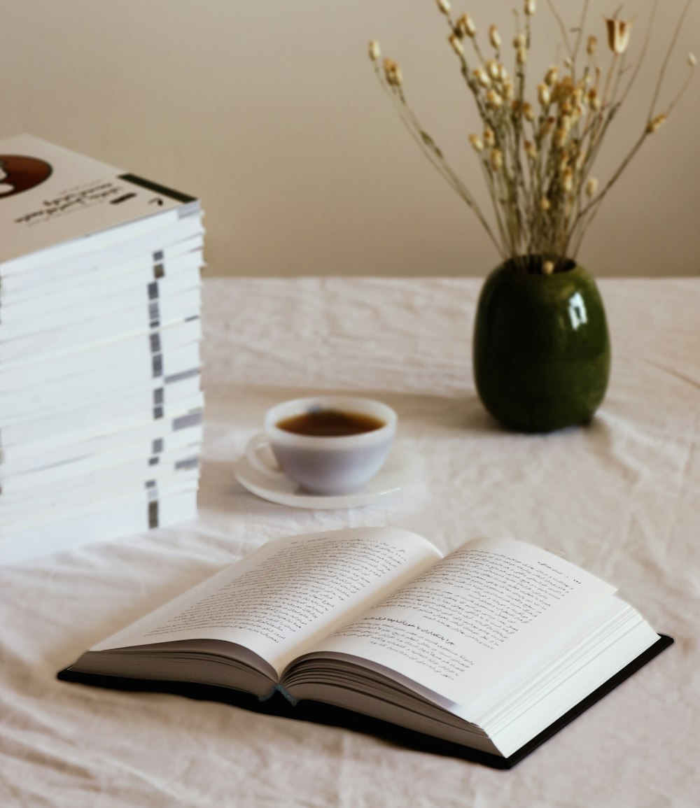 taza de cerámica blanca en platillo de cerámica blanca al lado del libro