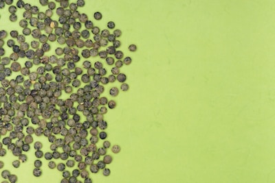 Shiny black peppercorns scattered on a dark wooden surface.
