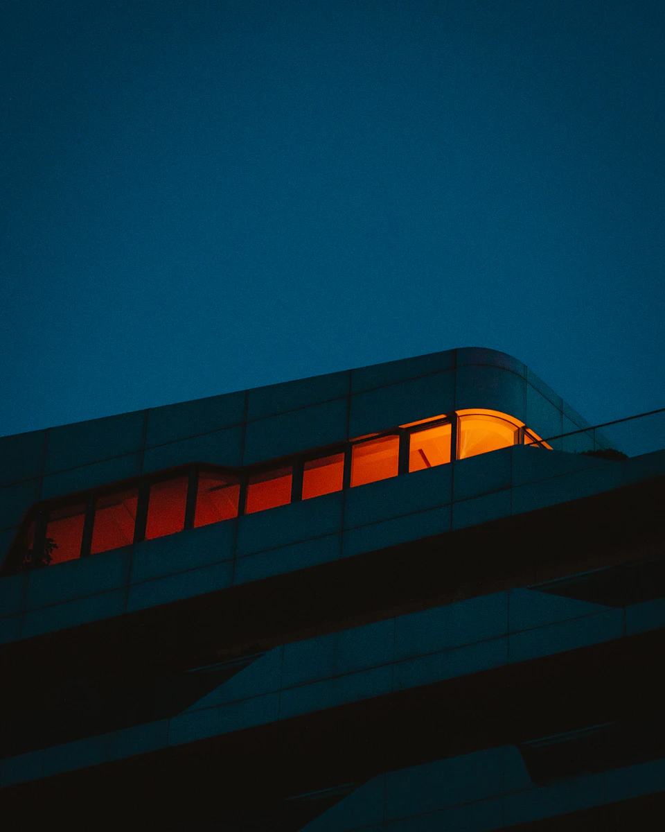 Curved modern building with illuminated window reflecting surroundings in warm orange light