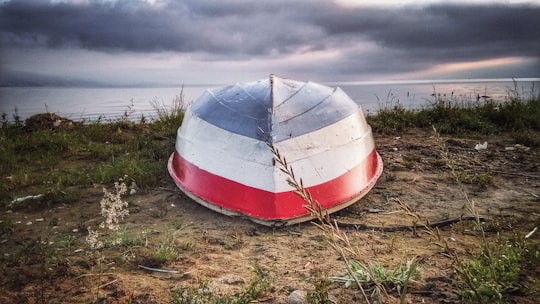 white and red boat on brown grass field under white clouds during daytime in Pogradec Albania