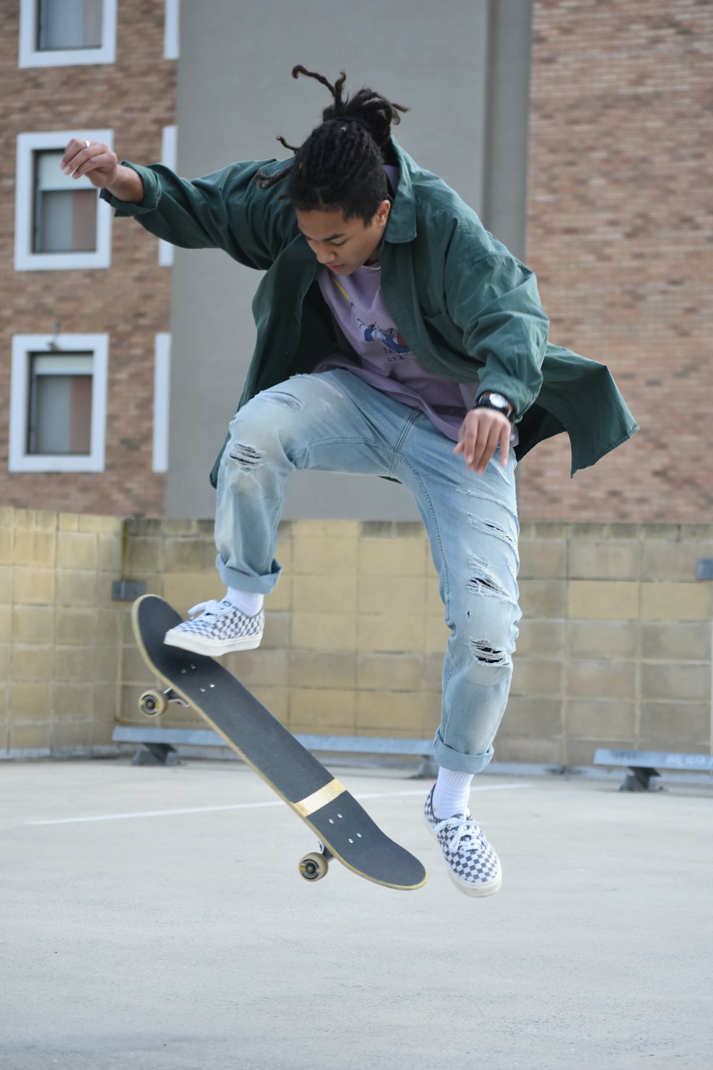 Mann in grünem Hoodie und blauer Jeans sitzt tagsüber auf dem Skateboard