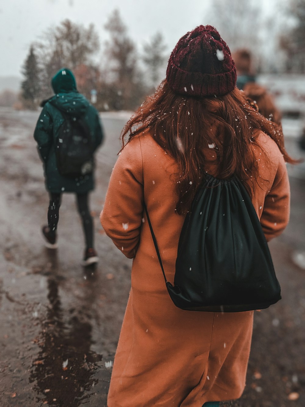 woman in black knit cap and brown coat walking on wet road during daytime