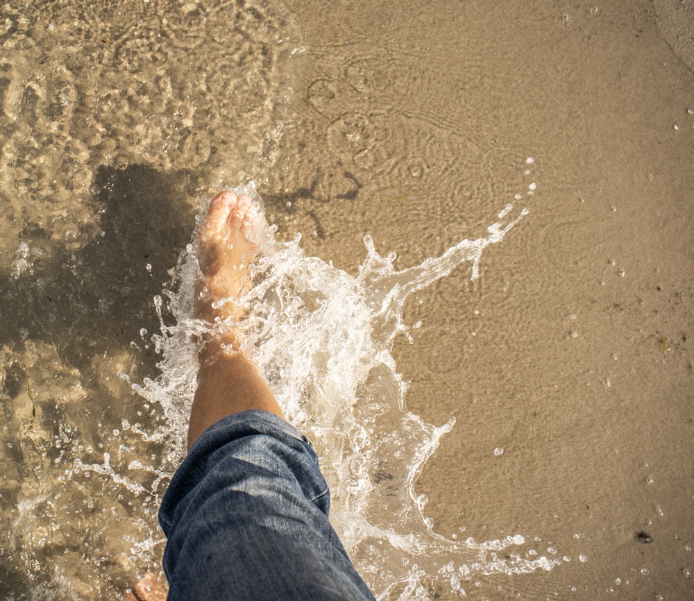 pessoa em jeans azuis em pé na areia marrom