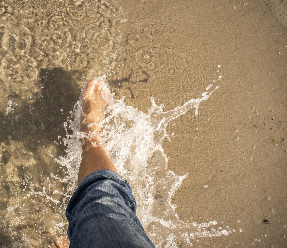 person in blue denim jeans standing on brown sand