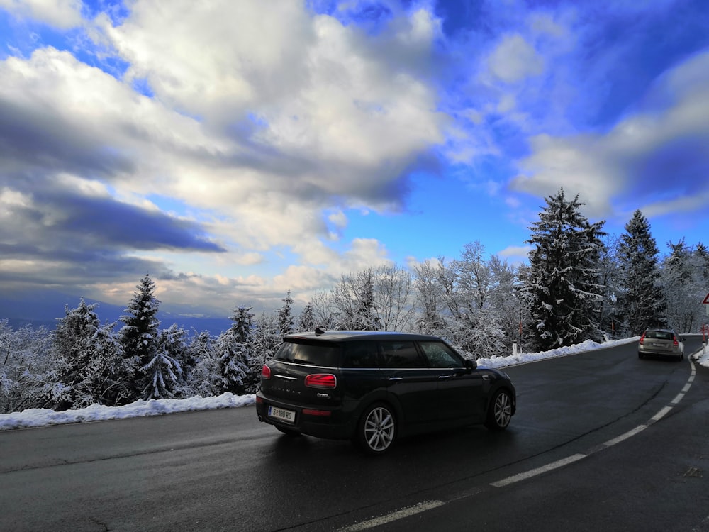 black suv on road near snow covered trees under blue sky and white clouds during daytime