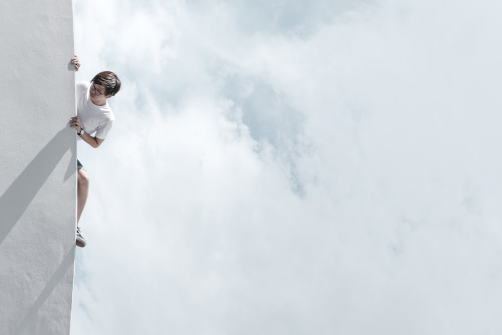 homem de camiseta branca e jeans azuis em pé sob nuvens brancas durante o dia