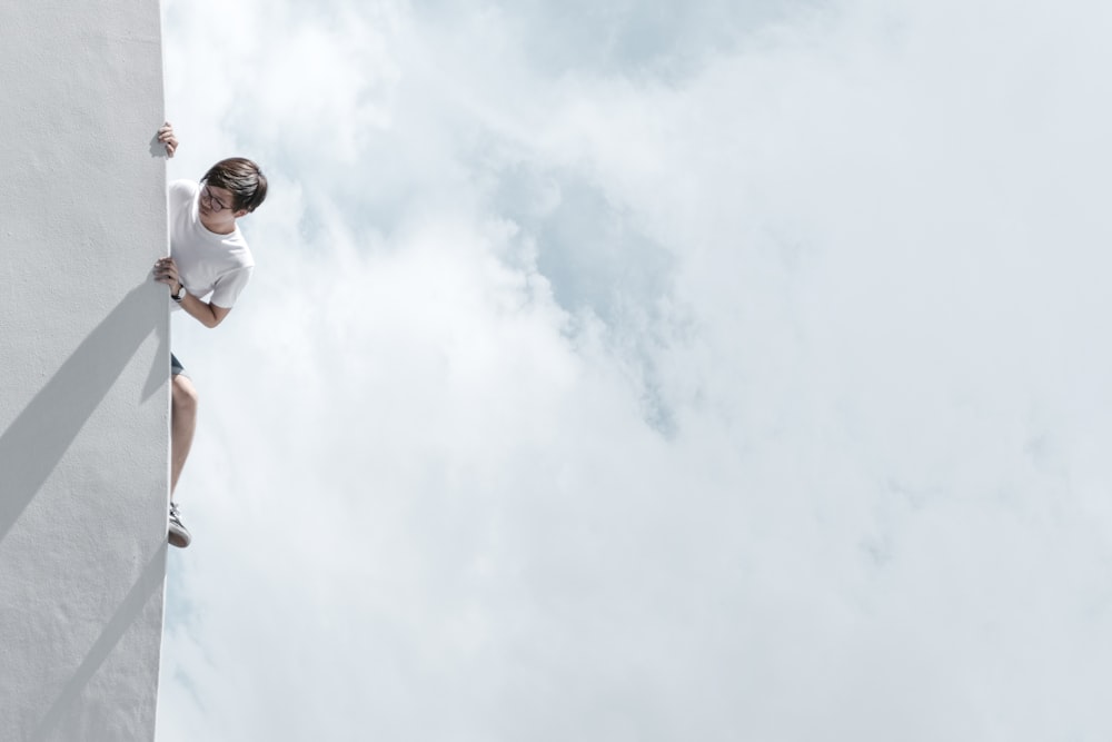 Mann in weißem T-Shirt und blauer Jeans steht tagsüber unter weißen Wolken