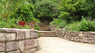 A serene garden pathway lined with earth-toned stones and lush plants.